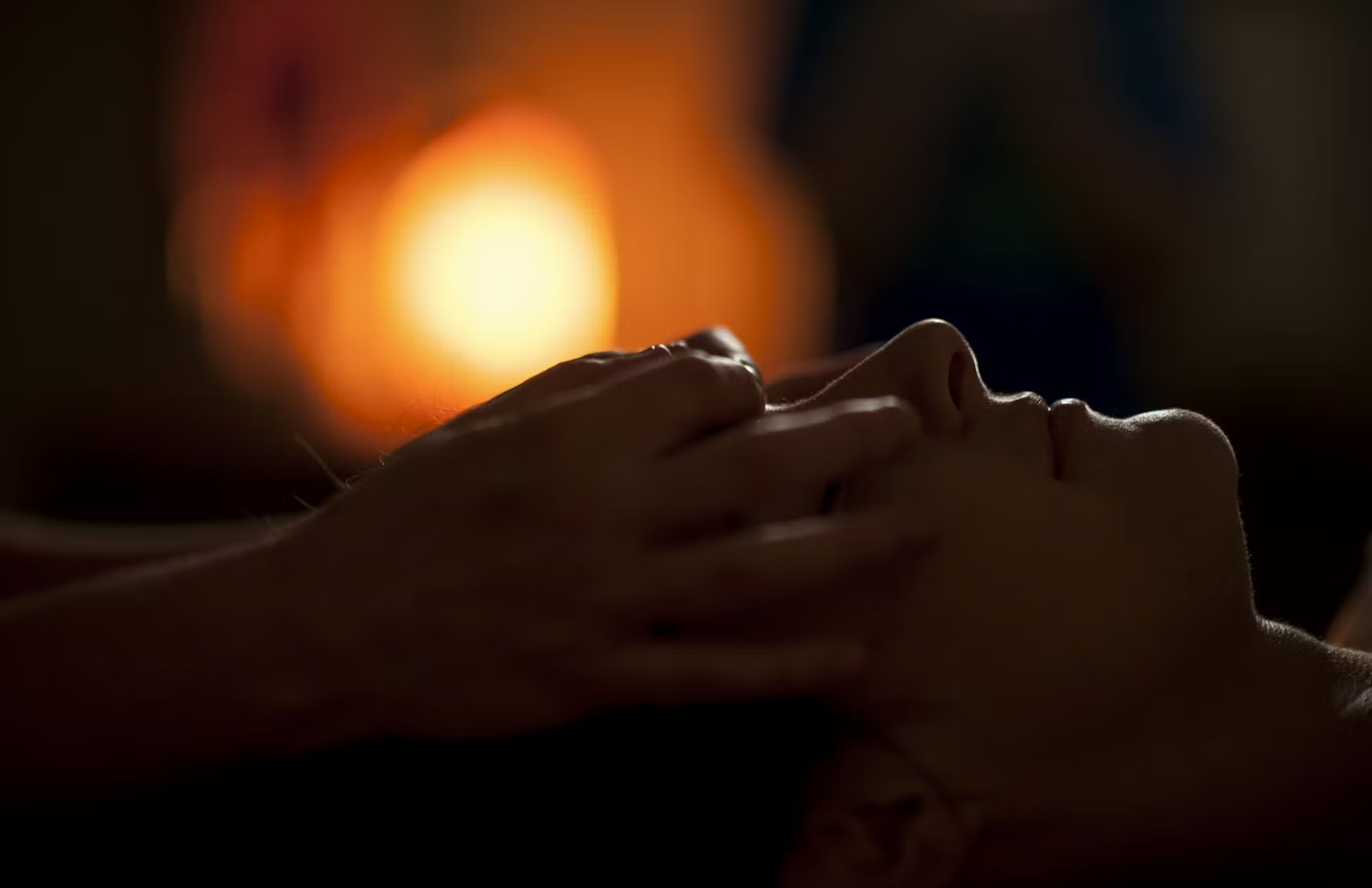 A client lying on the massage table in warm lamplight while Chelsea cradles their head